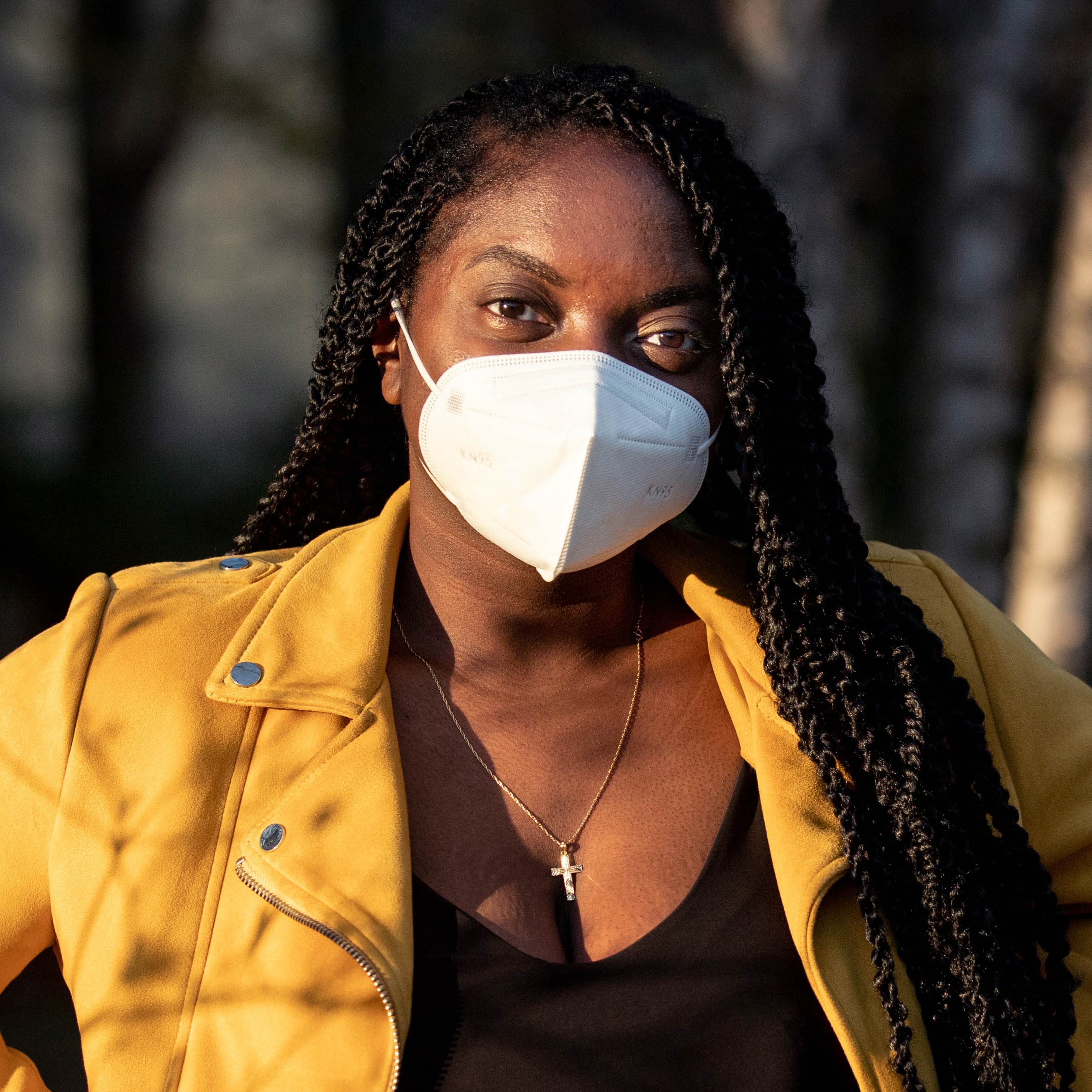 A young Black woman in a mask looking at the camera, wearing a dramatic yellow jacket.