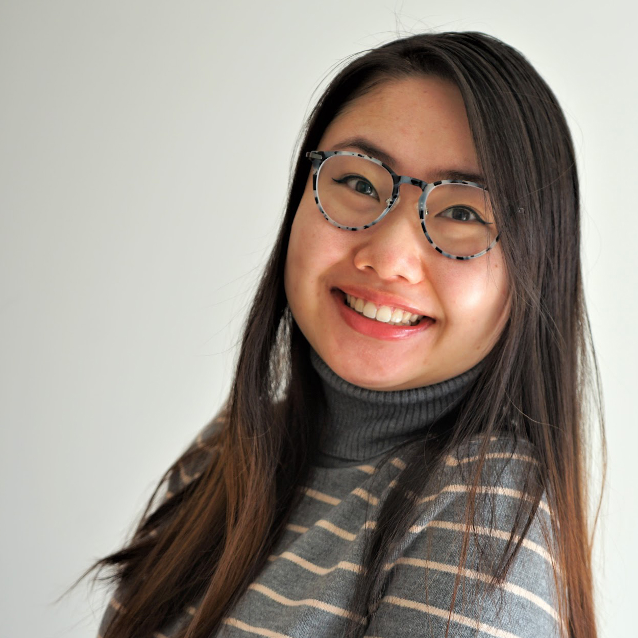 A young Asian woman with glasses smiles at the camera